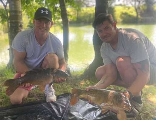 Friends enjoy a days fishing together. Two men in grey t-shirts display the fish they have caught.